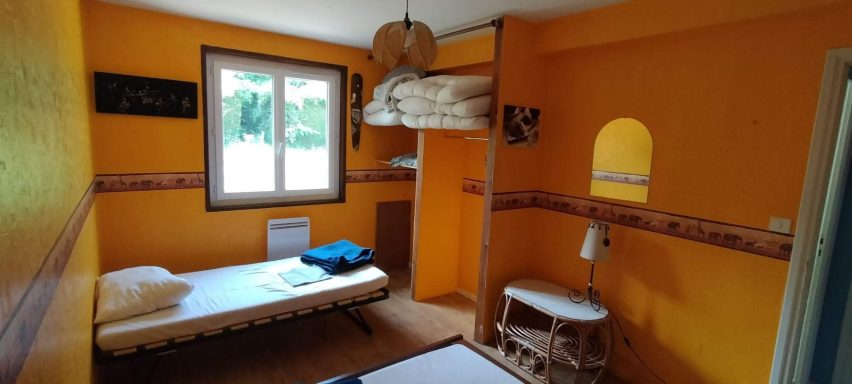 La chambre "africaine" Chambre lumineuse aux murs oranges, avec un lit, table et fenêtre donnant sur l'extérieur.