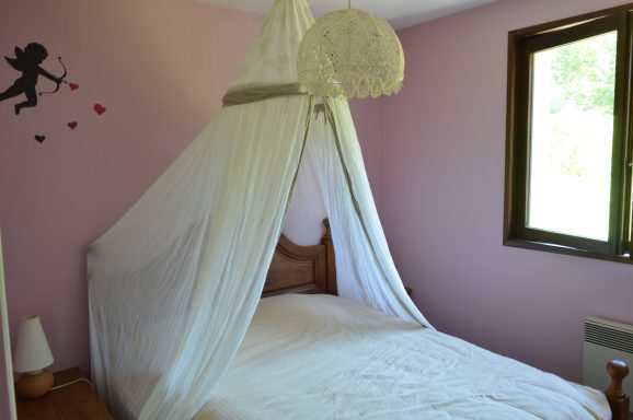 La chambre "baroque" Chambre avec lit sous une moustiquaire blanche et mur rose décoré, fenêtre ouverte.